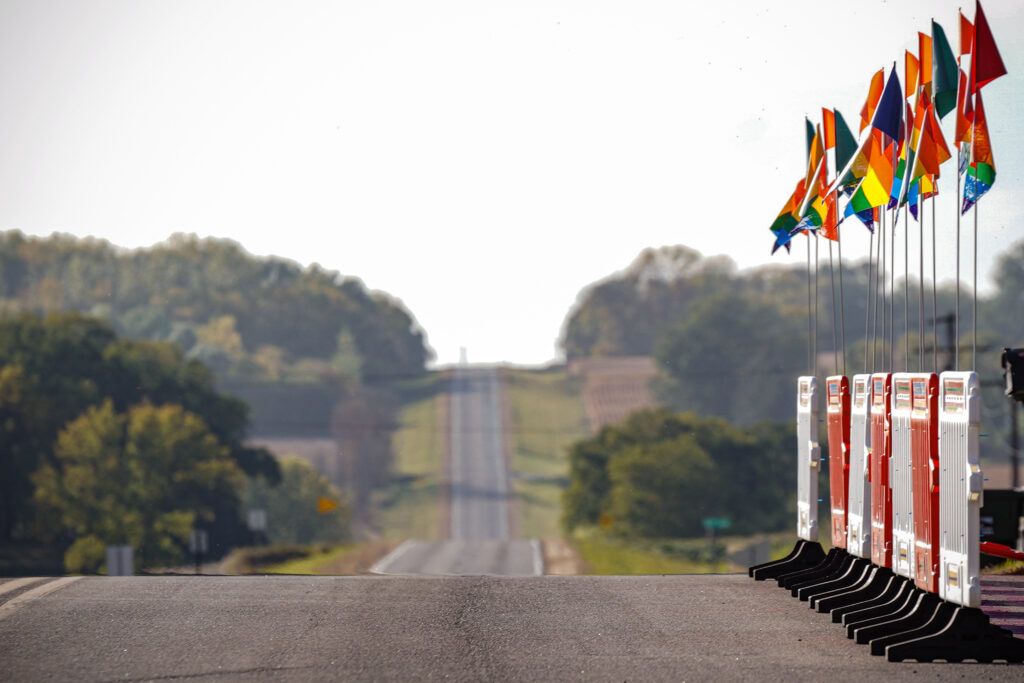 Image of empty rural highway and barricades on the right side that are topped with rainbow flags.