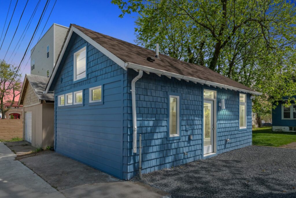 A blue shingled ADU with a pitched roof in the backyard of a home