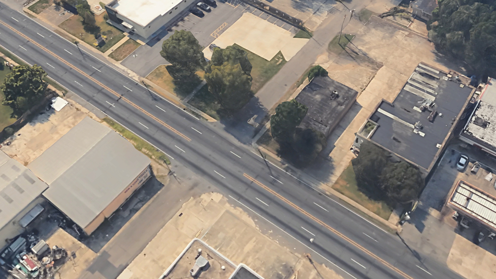 A one-lane road lined with a crumbling sidewalk intersects a wide, four-lane street
